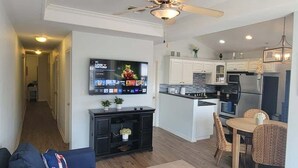 A modern kitchen with a central island, a dining area with a table and chairs, and a living room with a sofa and a TV mounted on the wall. - Cora Lee Beachview 2 Bedroom Condo (South Padre Island)