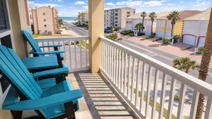A balcony with blue chairs, a view of a beach, and a street with buildings. - Cora Lee Beachview 2 Bedroom Condo (South Padre Island)