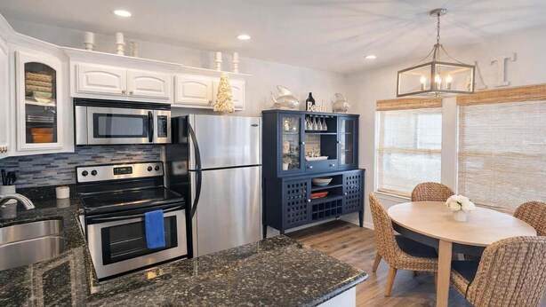 A modern kitchen with stainless steel appliances, a dark blue cabinet, and a dining area with wicker chairs. - Cora Lee Beachview 2 Bedroom Condo (South Padre Island)