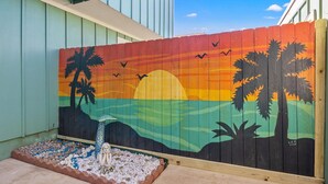Un mural colorido en una valla de madera que muestra un atardecer con palmeras y pájaros.