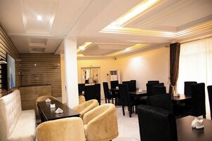Un salón de conferencias de hotel con diseño moderno, que presenta una mezcla de sillas negras y beige, una mesa central y una escalera que conduce a otra zona.