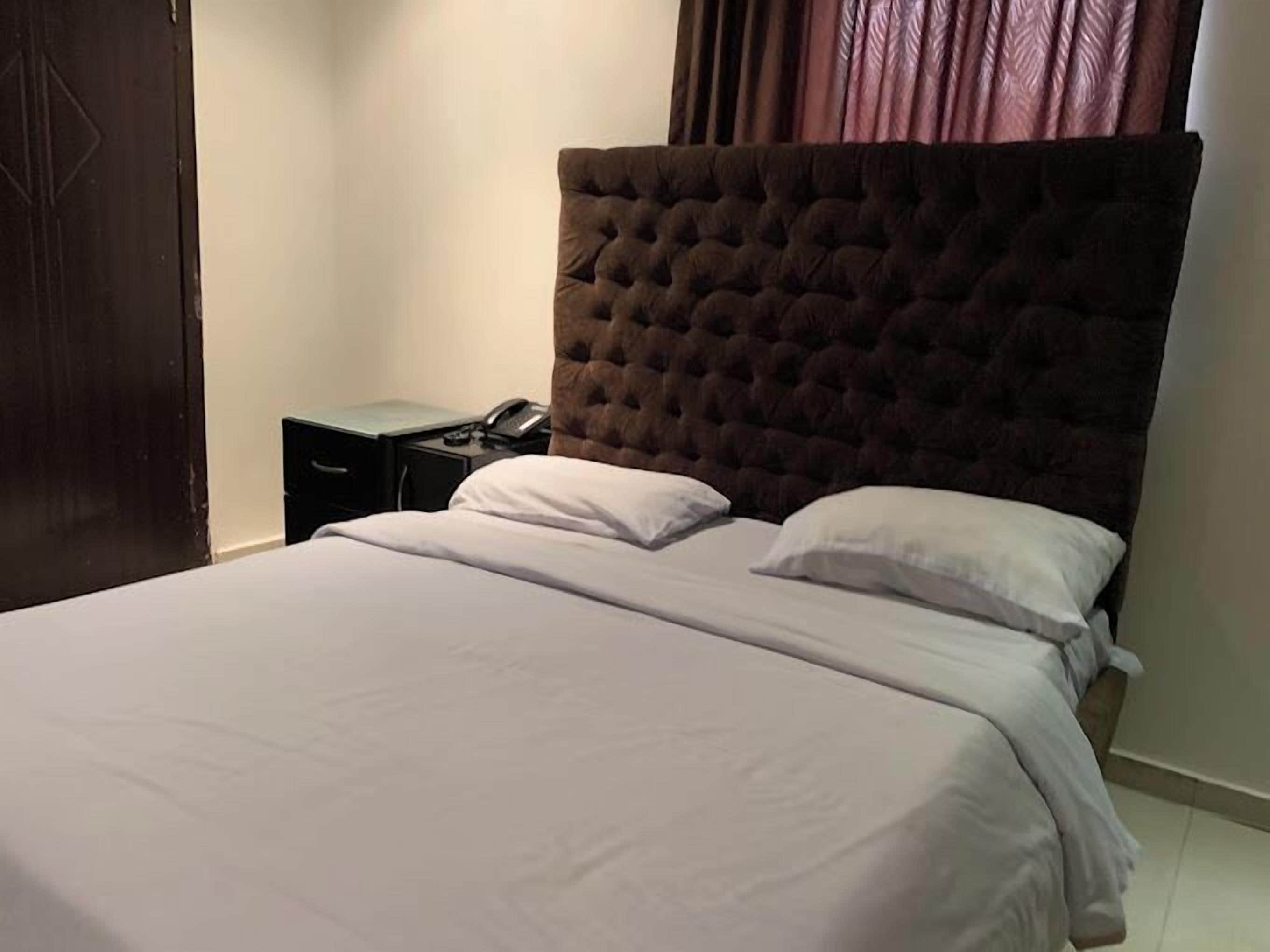 Una cama bien hecha con cabecera capitonada, una mesita de noche con lámpara y teléfono.