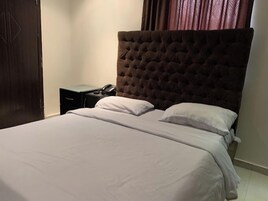 Una cama bien hecha con cabecera capitonada, una mesita de noche con lámpara y teléfono.