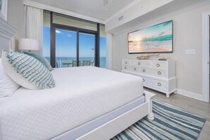 A bedroom with a large bed, a dresser, a painting, and a view of the ocean. - Phoenix Gulf Shores Ii 2003 3 Bedroom Condo (Gulf Shores)