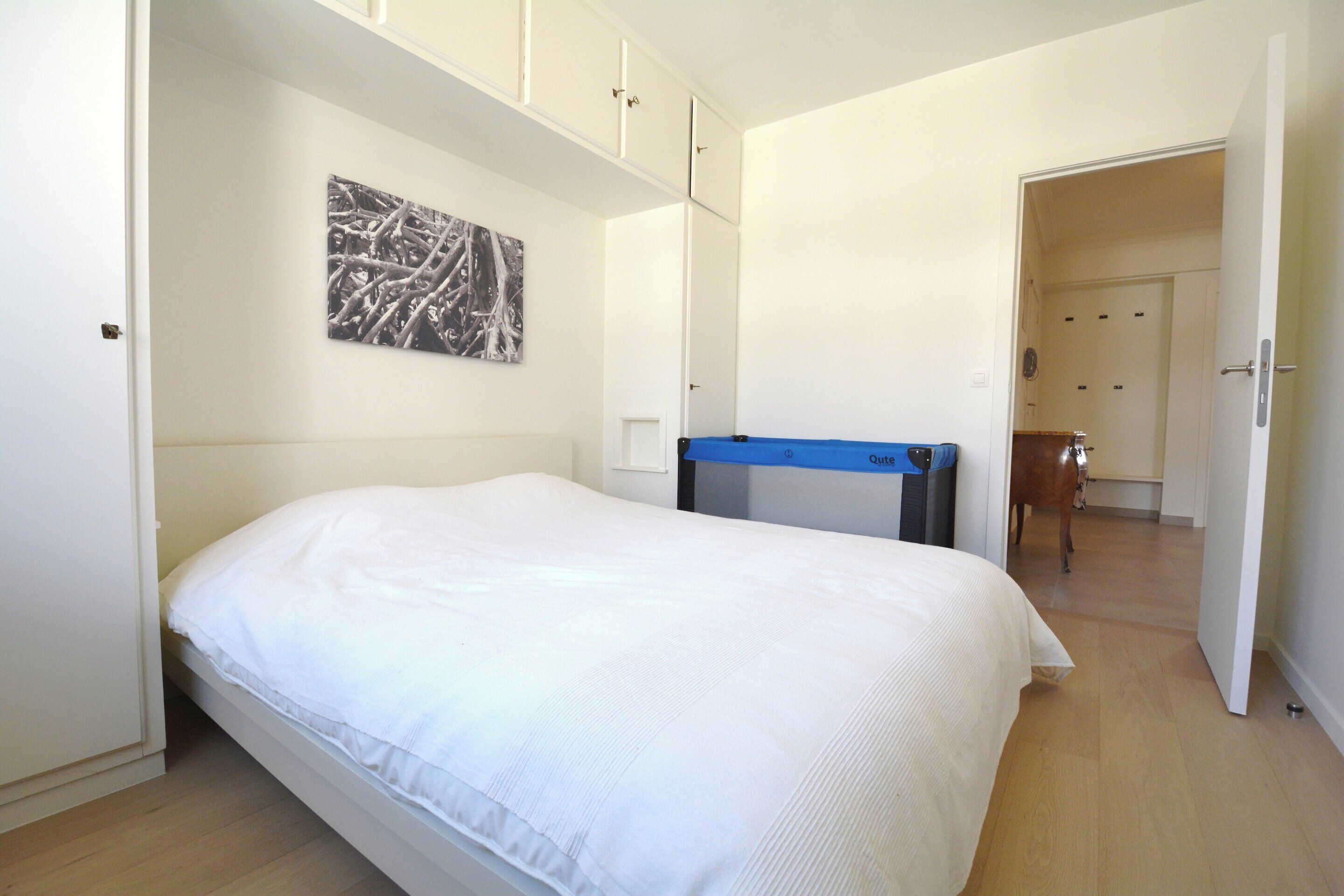 A bedroom with a bed, a desk, and a door leading to another room.