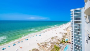 A beach view from a high-rise building with a pool and a beach with umbrellas. - Phoenix Gulf Shores Ii 1604 3 Bedroom Condo (Gulf Shores)