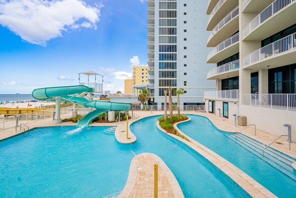 A swimming pool with a water slide and a view of a tall building in the background. - Phoenix Gulf Shores Ii 1604 3 Bedroom Condo (Gulf Shores)