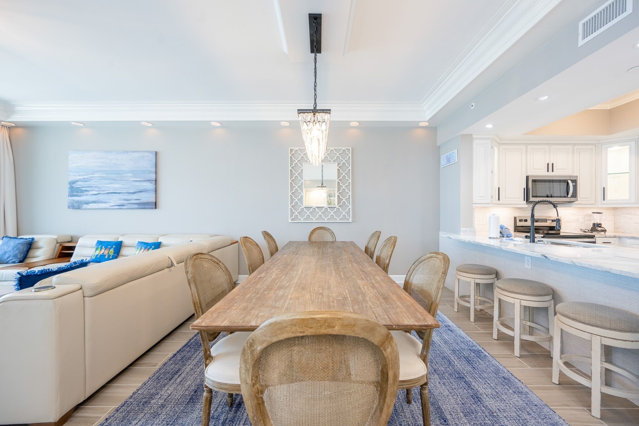 Una cocina moderna con armarios blancos, una isla central y un comedor con mesa y sillas de madera.