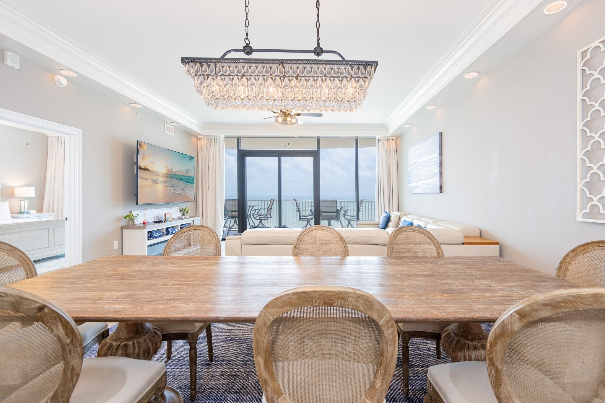 A spacious dining area with a large wooden table, wicker chairs, and a chandelier.