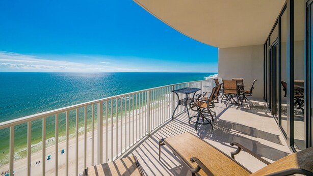 A balcony with a view of the ocean, furnished with chairs and a table. - Phoenix Gulf Shores Ii 2104 3 Bedroom Condo (Gulf Shores)