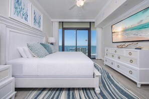 Ein Schlafzimmer mit Bett, Schminktisch, Fernseher und einem Balkon mit Meerblick.