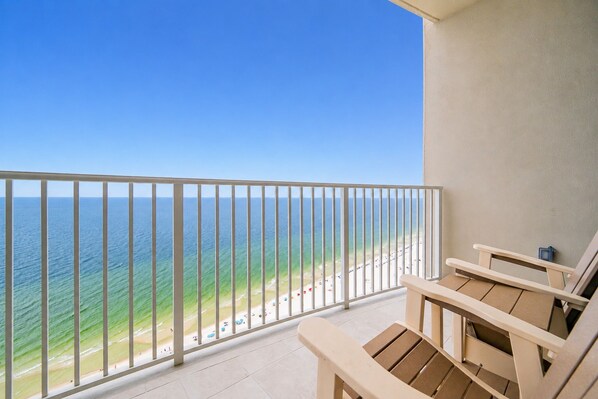 Un balcón con vista al océano y a la playa, sillas de madera y piso de baldosas.