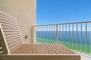 A balcony with a view of the ocean, a wooden bench, and a wall-mounted light fixture.