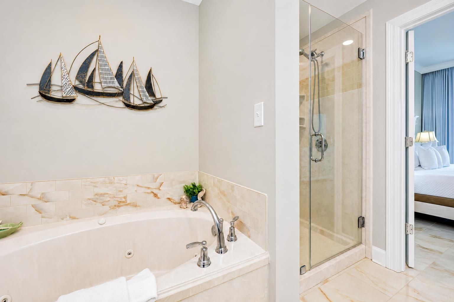 A bathroom with a bathtub, a glass-enclosed shower, and a bed visible through an open door.