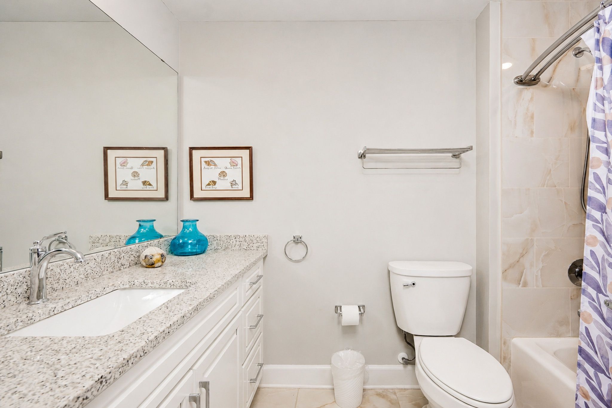 Une salle de bain avec un lavabo, des toilettes et une douche. Deux tableaux encadrés sont accrochés au mur.