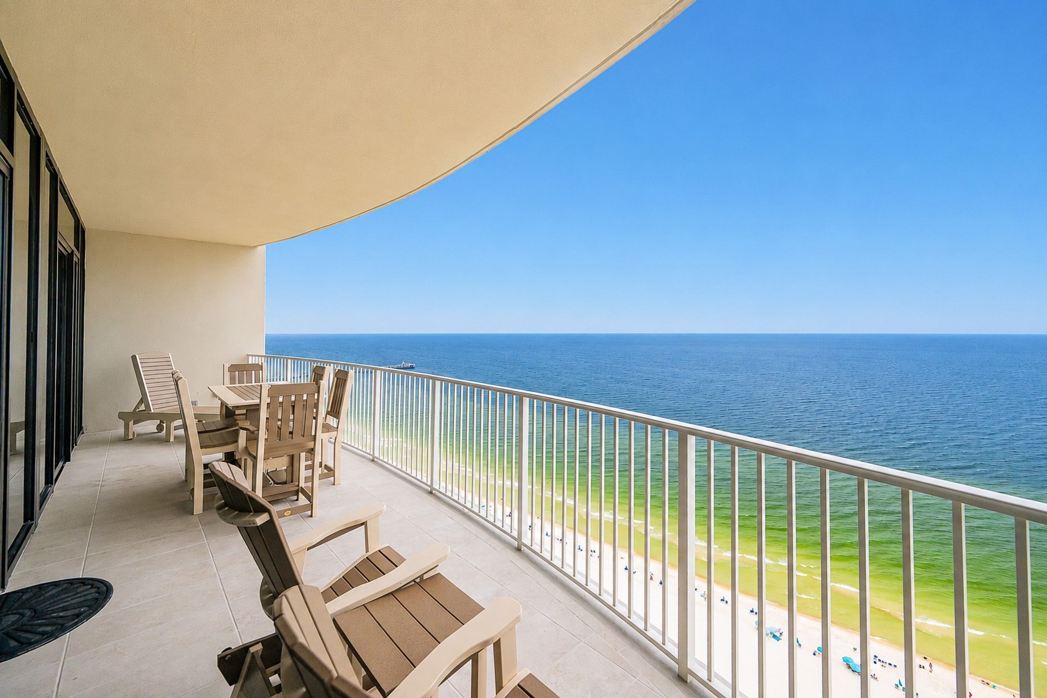 A balcony with a view of the ocean, equipped with wooden chairs and a table.