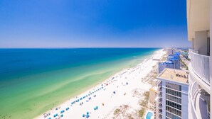 A beach view with a clear sky, a sandy beach, and a building with balconies overlooking the ocean. - Phoenix Gulf Shores Ii 2504 3 Bedroom Condo (Gulf Shores)