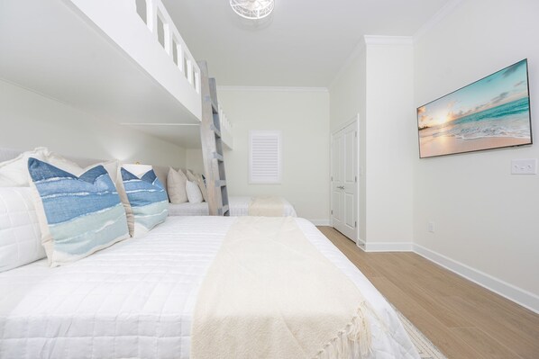 A bedroom with a bed, a ladder, a painting of a beach scene, and a door. - Phoenix Gulf Shores Ii 2504 3 Bedroom Condo (Gulf Shores)