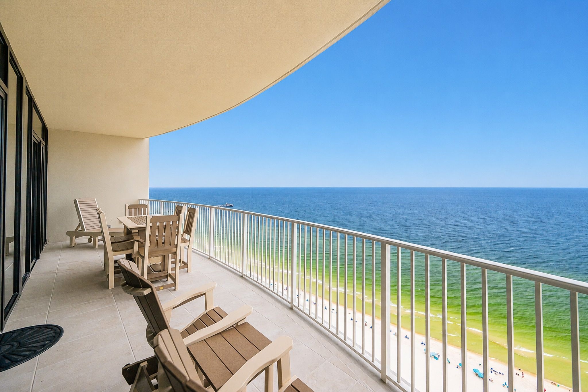 A balcony with a view of the ocean, equipped with wooden chairs and a table.