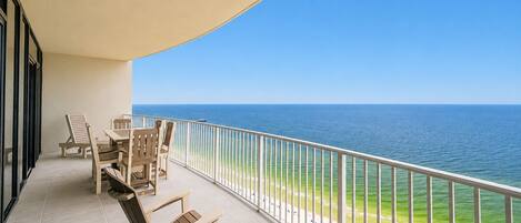 A balcony with a view of the ocean, equipped with wooden chairs and a table.