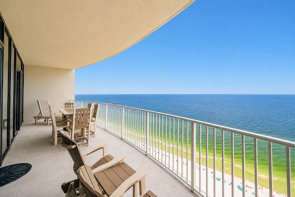 A balcony with a view of the ocean, equipped with wooden chairs and a table. - Phoenix Gulf Shores Ii 2303 3 Bedroom Condo (Gulf Shores)