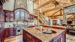 A spacious kitchen with a large island, wooden cabinets, and a stone accent wall. - Bridge To Solitude 6 Bedroom Home (Breckenridge)