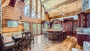 A spacious log cabin interior with a large dining area, a kitchen with dark wood cabinets, and a stone accent wall. - Bridge To Solitude 6 Bedroom Home (Breckenridge)