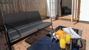A black outdoor sofa on a brick patio with a table beside it, holding croissants, juice, and a newspaper. - The Baler House (Hayle)