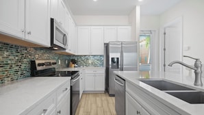 A modern kitchen with white cabinets, a stainless steel refrigerator, a microwave, and a tiled backsplash.