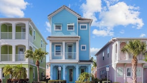 A row of colorful, multi-story houses with balconies, a clear blue sky, and palm trees.