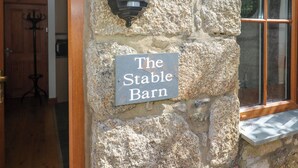 Un muro de piedra con un letrero que dice "The Stable Barn" y un farol negro.