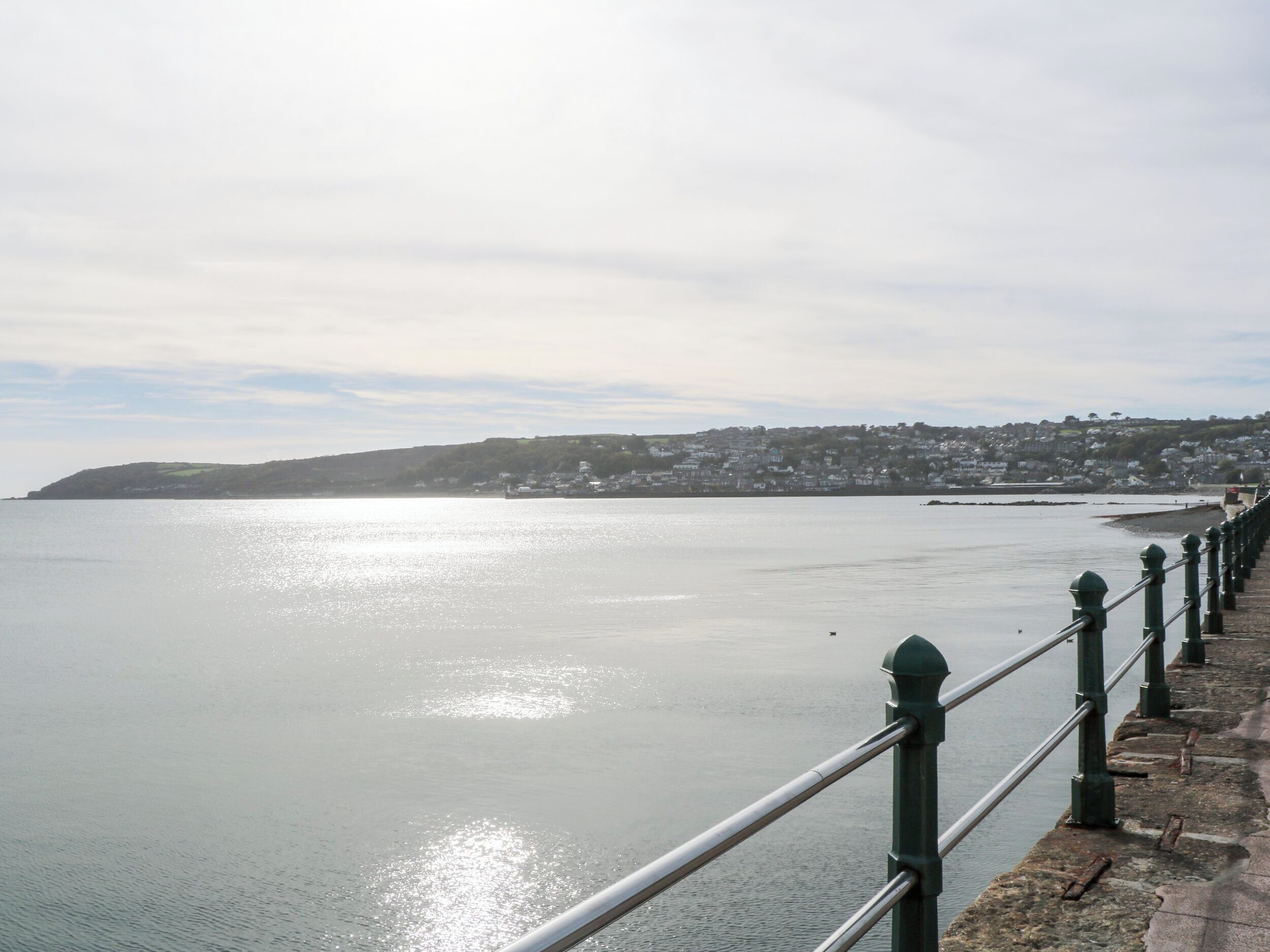 A coastal view with a stone promenade and a metal railing.