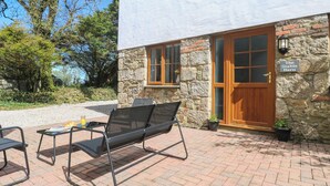 Un edificio de piedra con puerta y ventanas de madera, un letrero que dice “The Stable Barn”, y un patio con una silla y una mesa de metal.