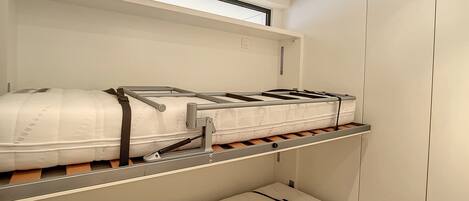 A bunk bed with a mattress on the top bunk and a single bed on the bottom.