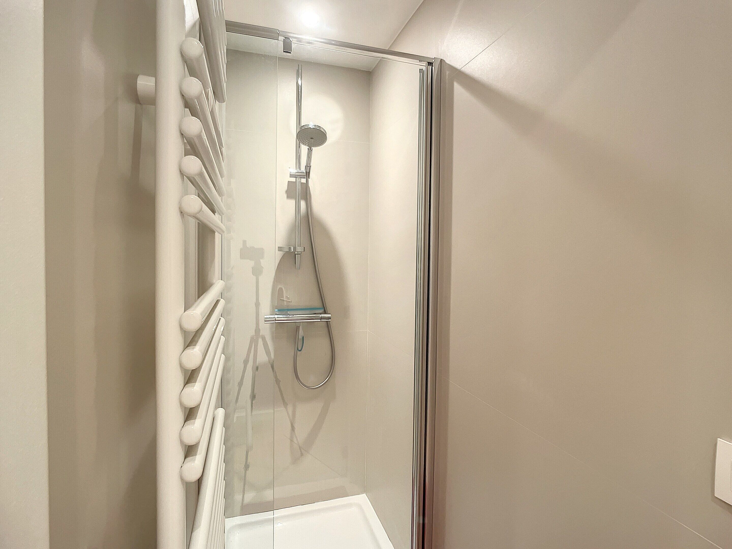 A modern shower with a glass enclosure, a handheld showerhead, and a glass seat.
