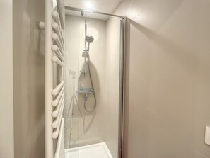 A modern shower with a glass enclosure, a handheld showerhead, and a glass seat.