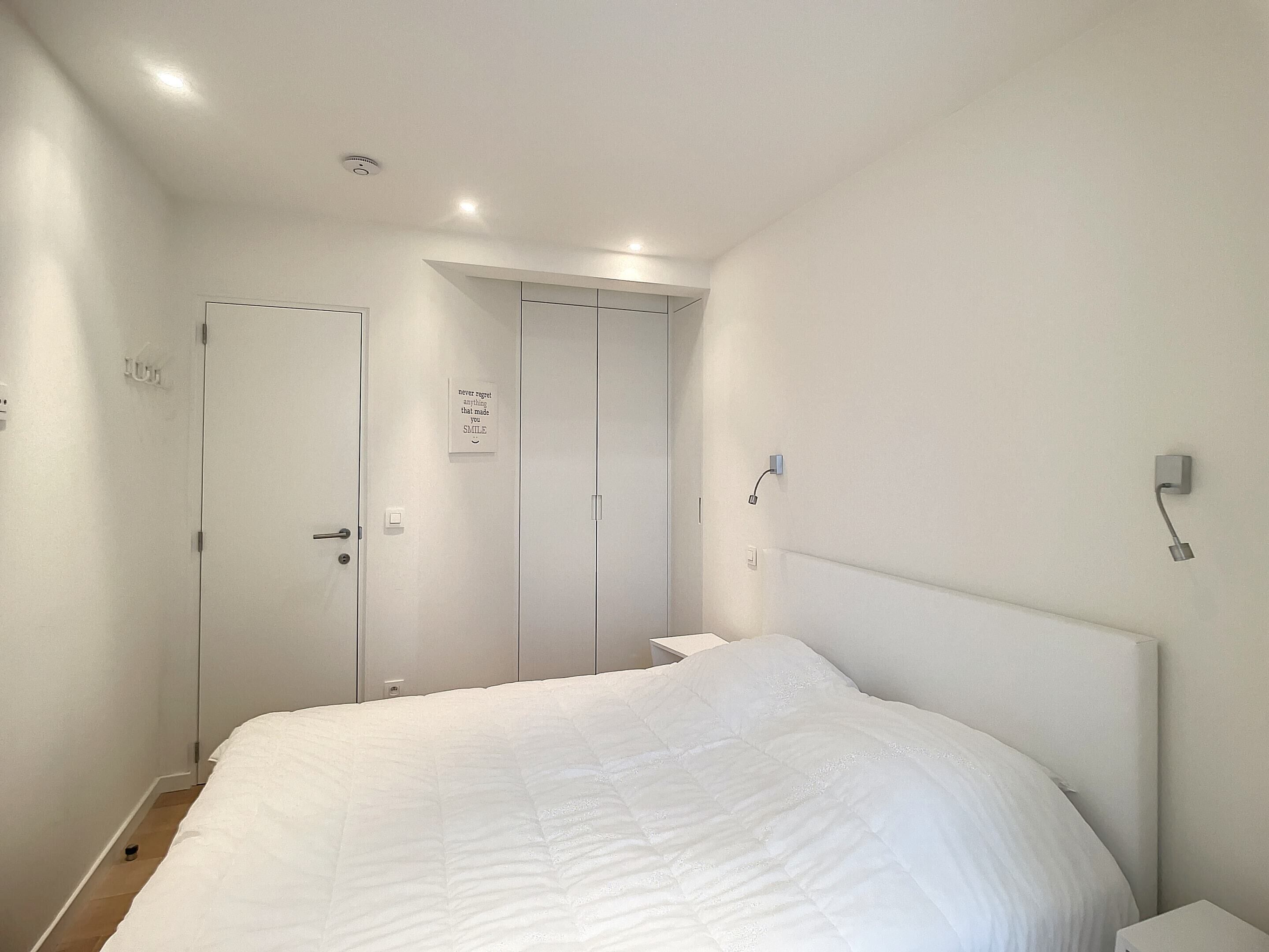 A bedroom with a large bed, a wardrobe, and a door with a motivational sign.