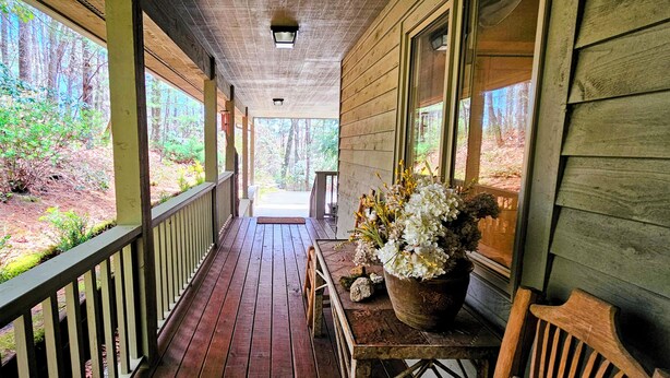 Eine hölzerne Veranda mit Backsteinboden, einem Geländer und einem Blumentopf mit weißen Blüten.
