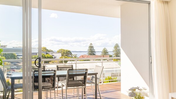 A balcony with a table and chairs, overlooking a body of water and buildings.