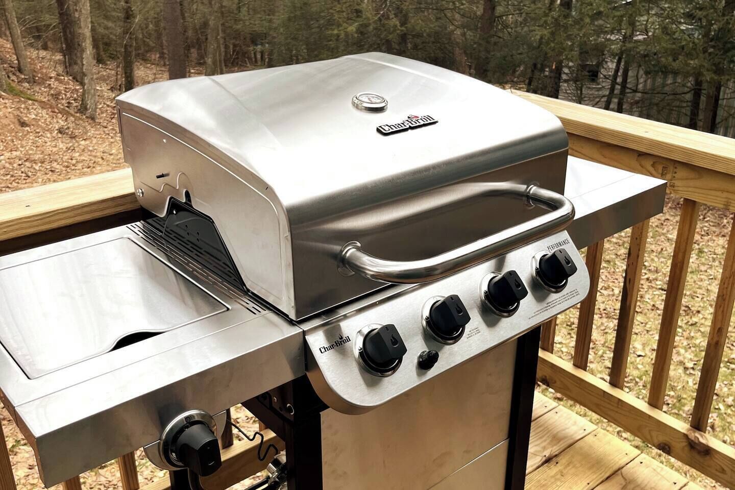 A Char-Broil gas grill with four burners and a side burner, mounted on a wooden deck with a view of trees.