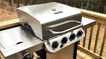 A Char-Broil gas grill with four burners and a side burner, mounted on a wooden deck with a view of trees.