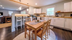 A modern kitchen with white cabinets, a wooden dining table, and pendant lighting. - Bright, Spotless Cottage Near Bethel Woods (Highland)