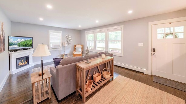 A living room with a fireplace, sofa, TV, and a wooden table with baskets. - Bright, Spotless Cottage Near Bethel Woods (Highland)