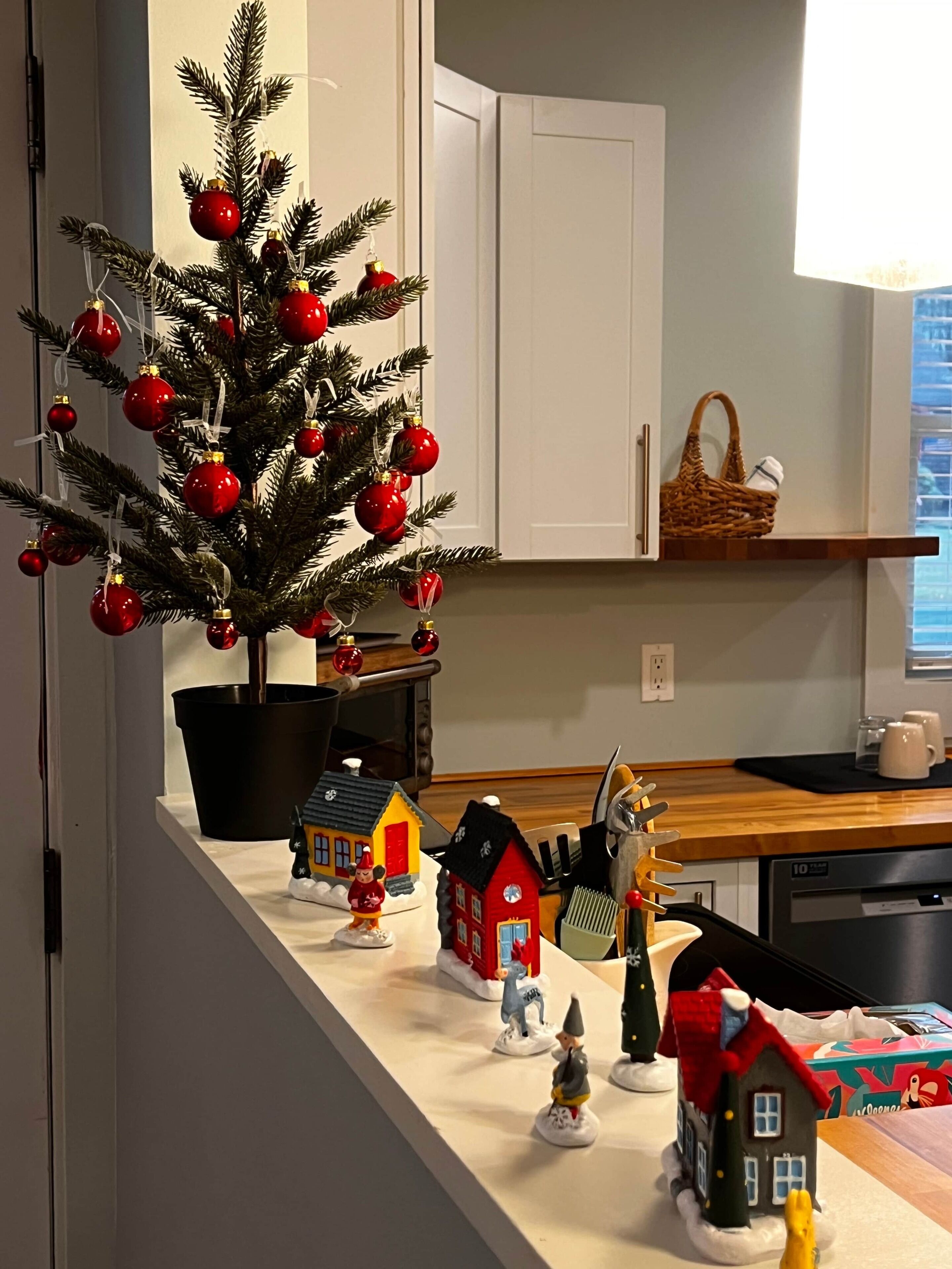 Un comptoir de cuisine décoré d’un sapin de Noël, de petites maisons miniatures et d’un panier.