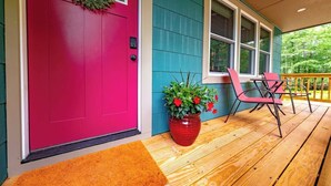 A wooden deck with a bright red door, a potted plant with red flowers, and a red chair. - Bright, Spotless Cottage Near Bethel Woods (Highland)