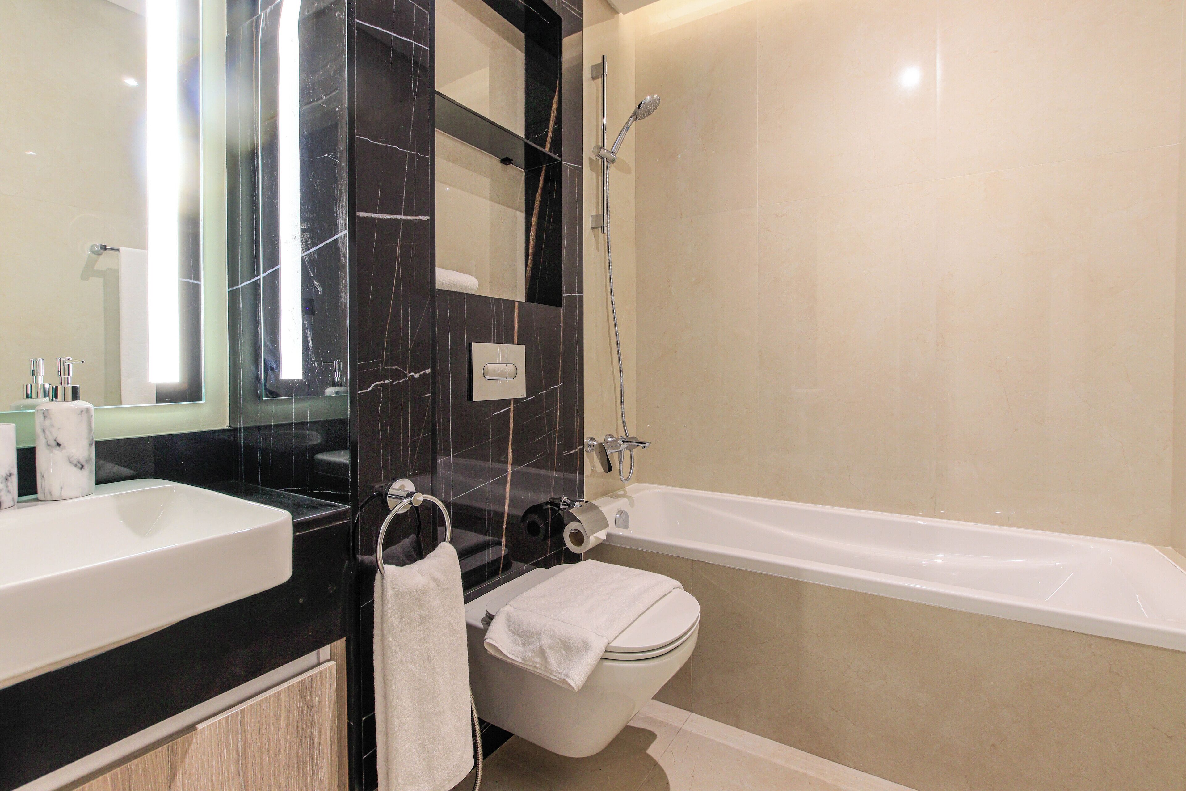 A modern bathroom with a black marble vanity, a white sink, a toilet, and a bathtub.