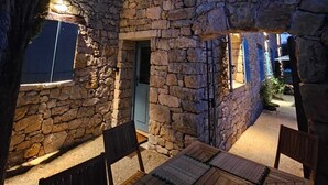 A stone building with a wooden deck and chairs, featuring a stone wall and a door.