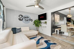 Una sala de estar moderna con un sofá, un televisor, un ventilador de techo y una zona de comedor.