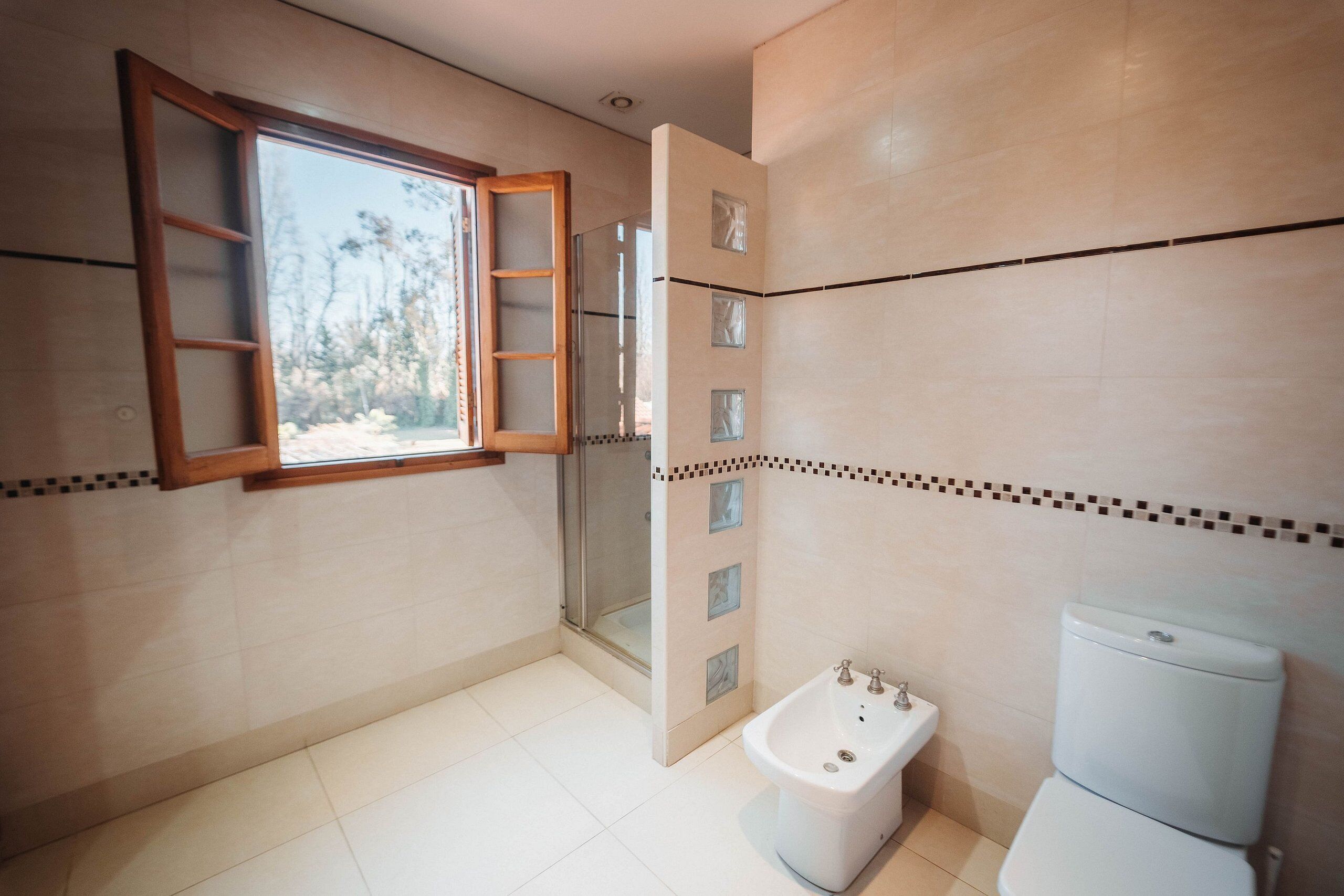 Un baño con ducha, inodoro y ventana de madera.