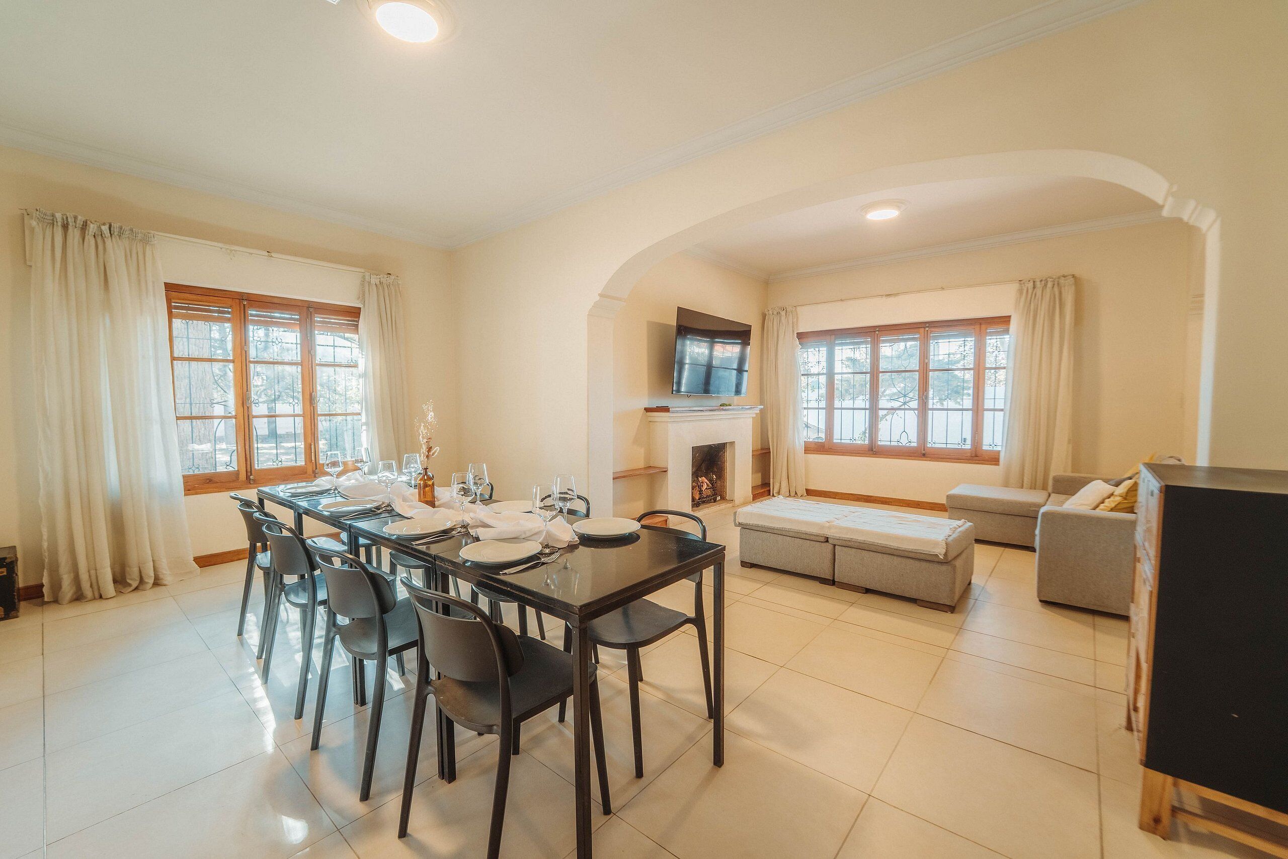 A dining area with a table set for four, a fireplace, and a sofa in a well-lit room with large windows.
